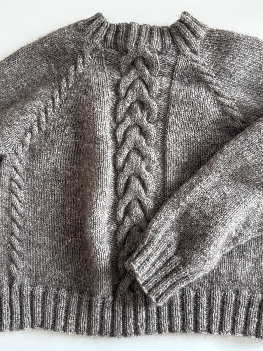 Liegender Pullover: großer geflochtener Mittelzopf und schmale Zöpfe entlang der Raglanlinien